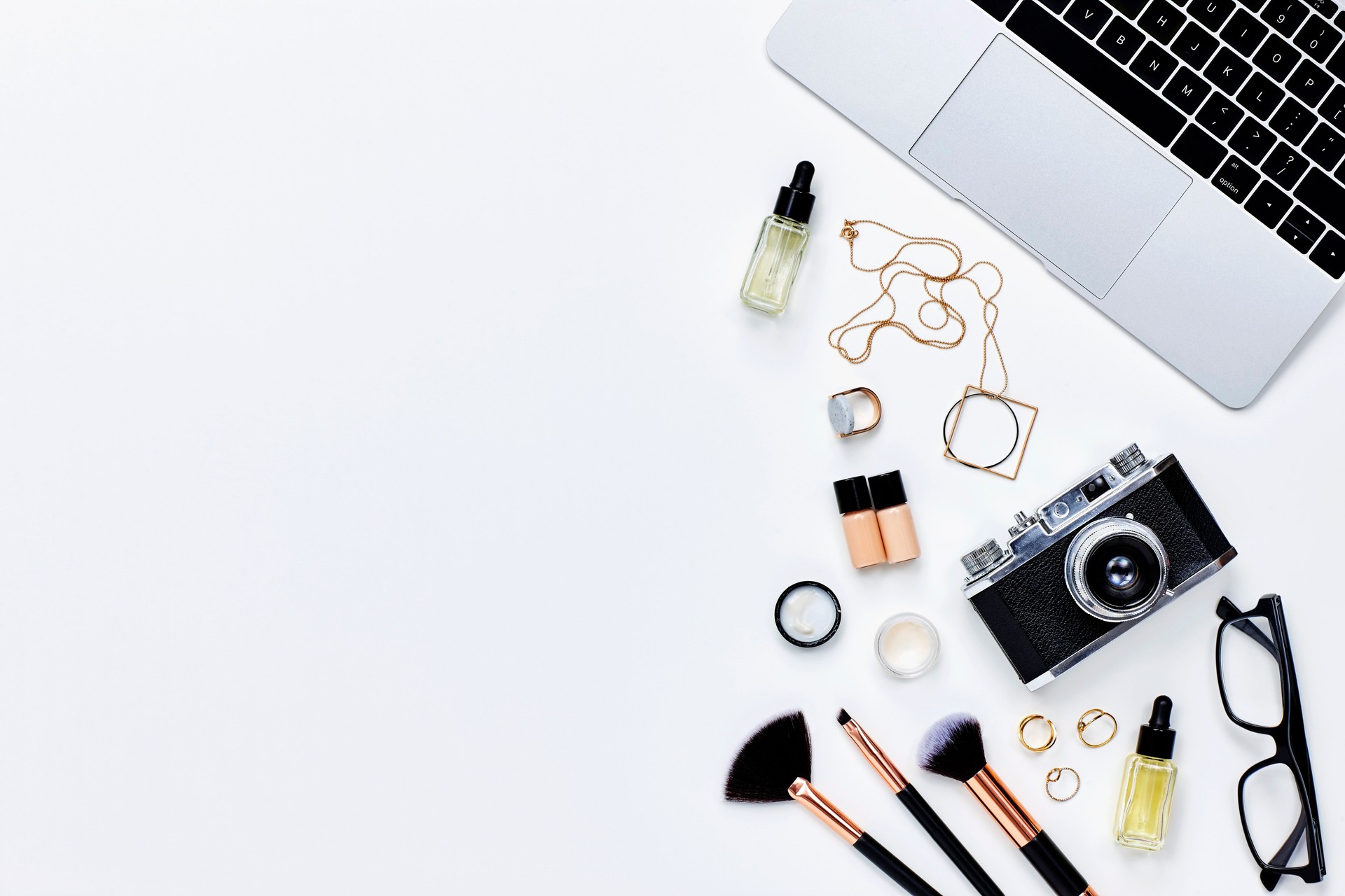 Various beauty products with camera and laptop on white background