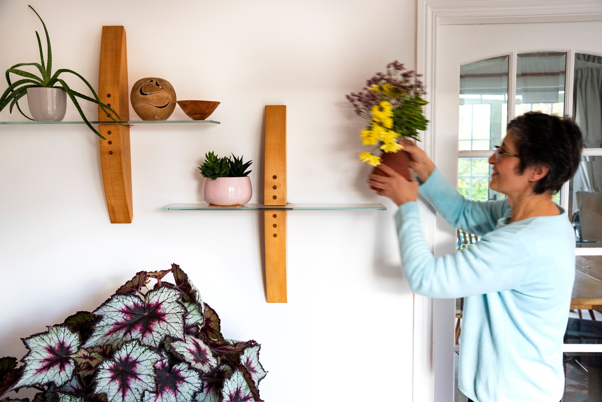 Woman placing fresh flowers on a shelves in a modern home - Stock photo
